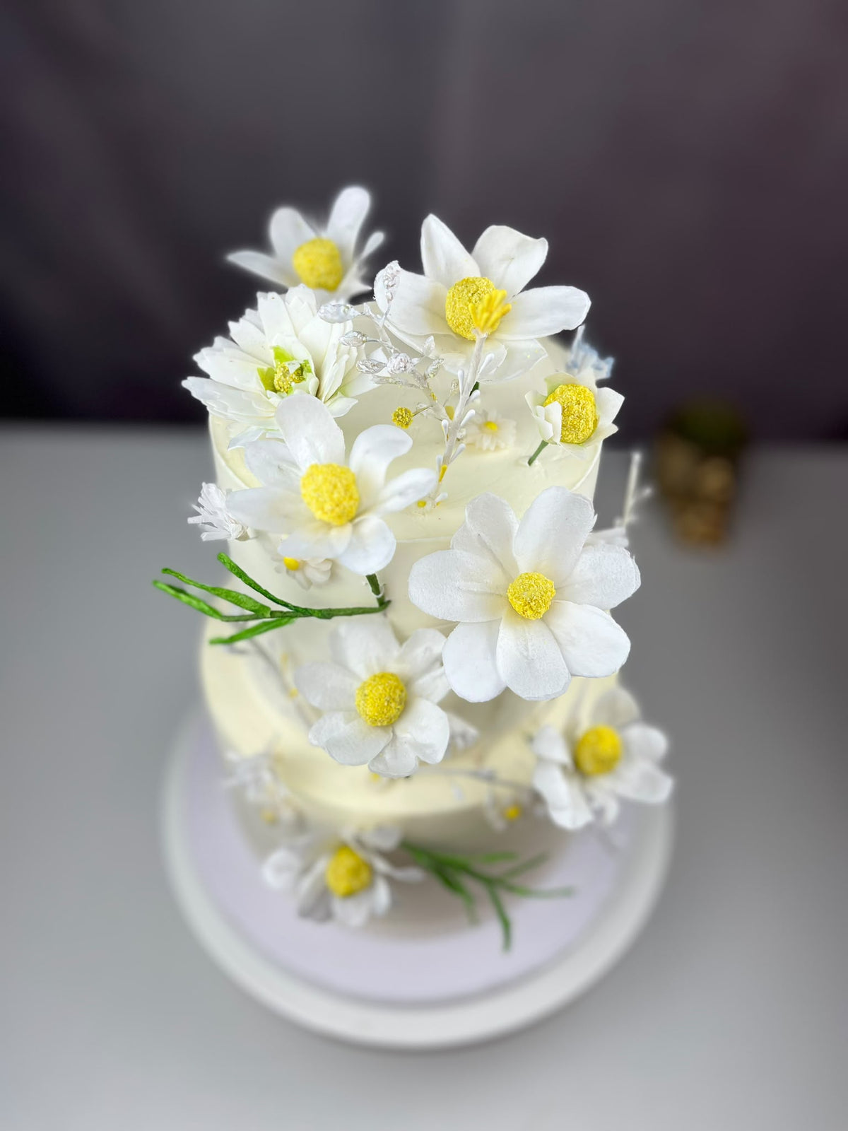 Edible wafer paper daisies with white petals and yellow centres on a floral two-tier cake.