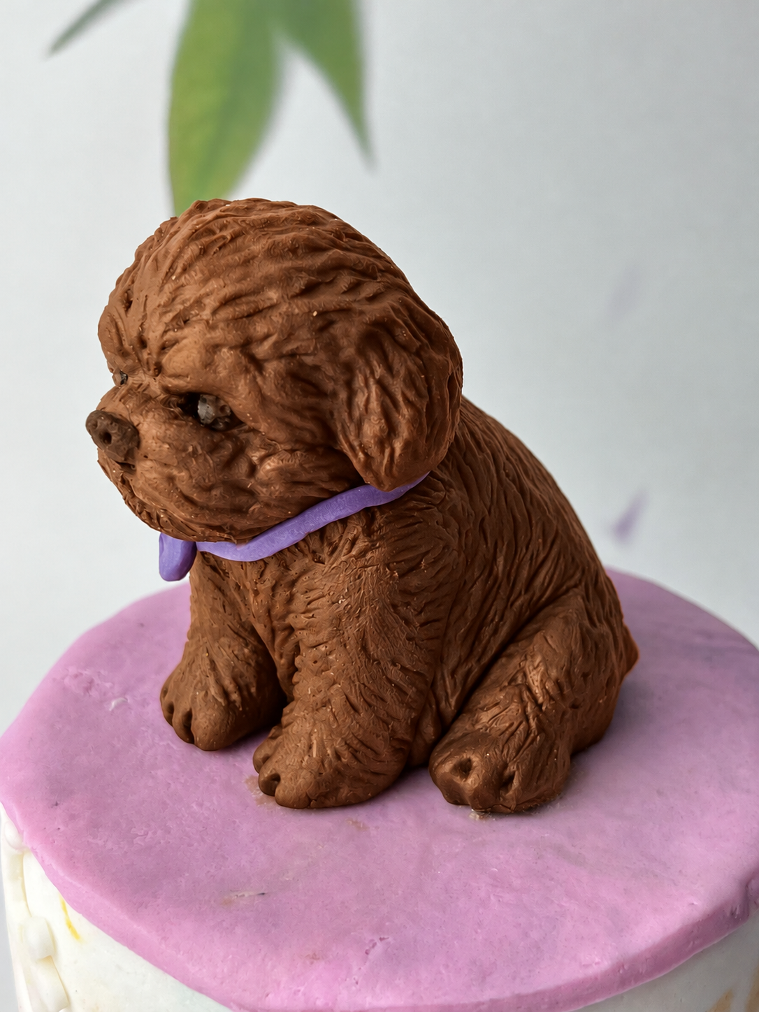 Brown handmade edible fondant dog cake topper with textured fur and purple collar on a pastel cake.