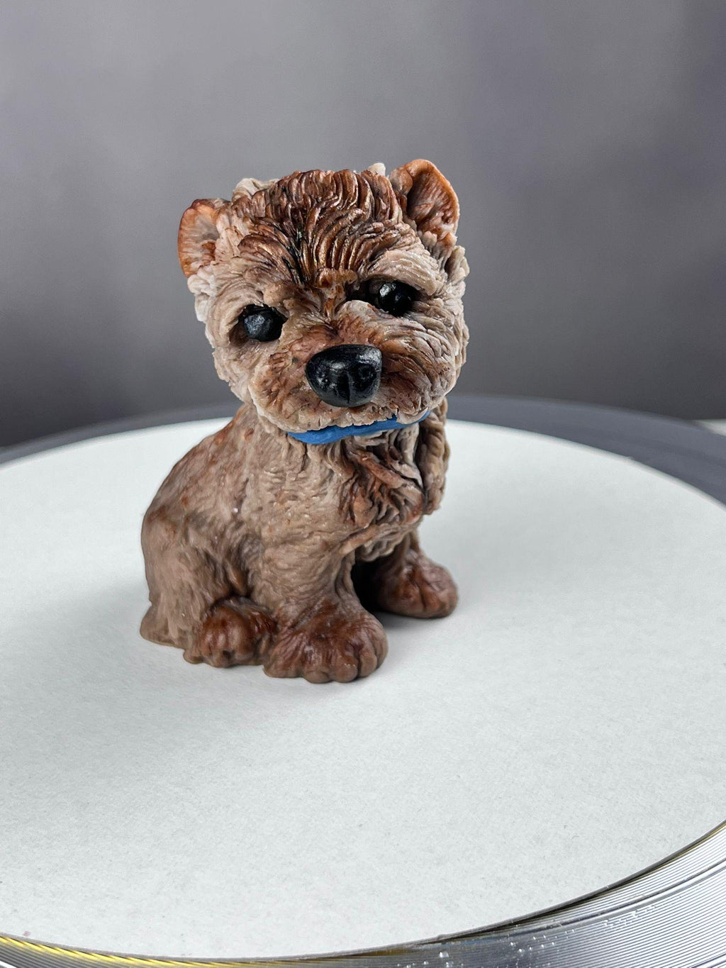 Brown edible fondant terrier dog cake topper with a blue bow, front view.