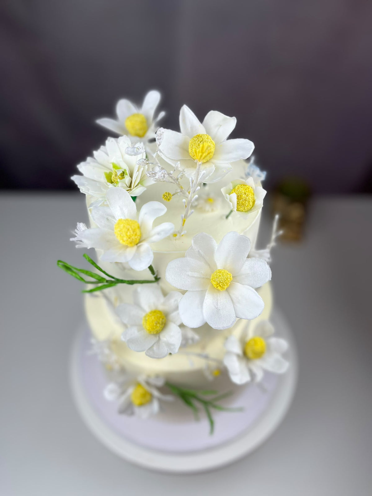 Close-up of white edible wafer paper daisies arranged on a pale celebration cake.
