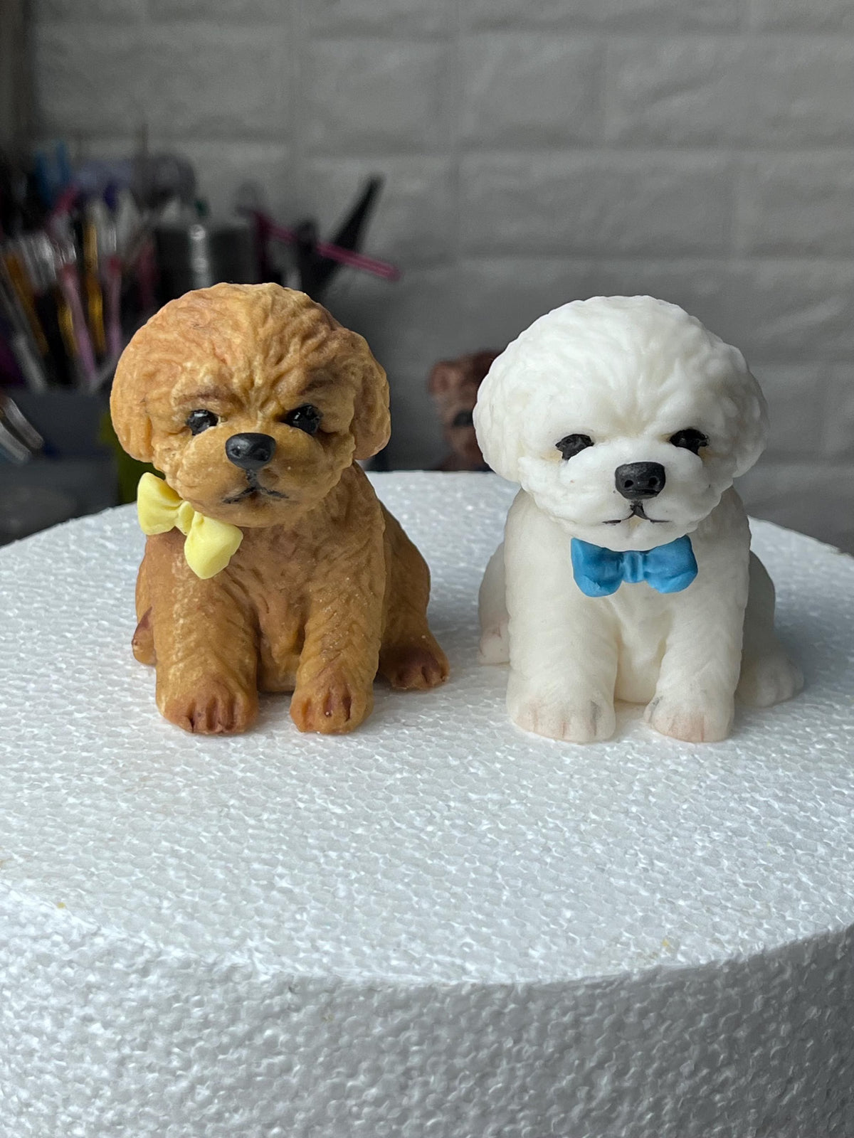 Brown and white edible fondant dog cake toppers with textured fur, wearing yellow and blue bows.