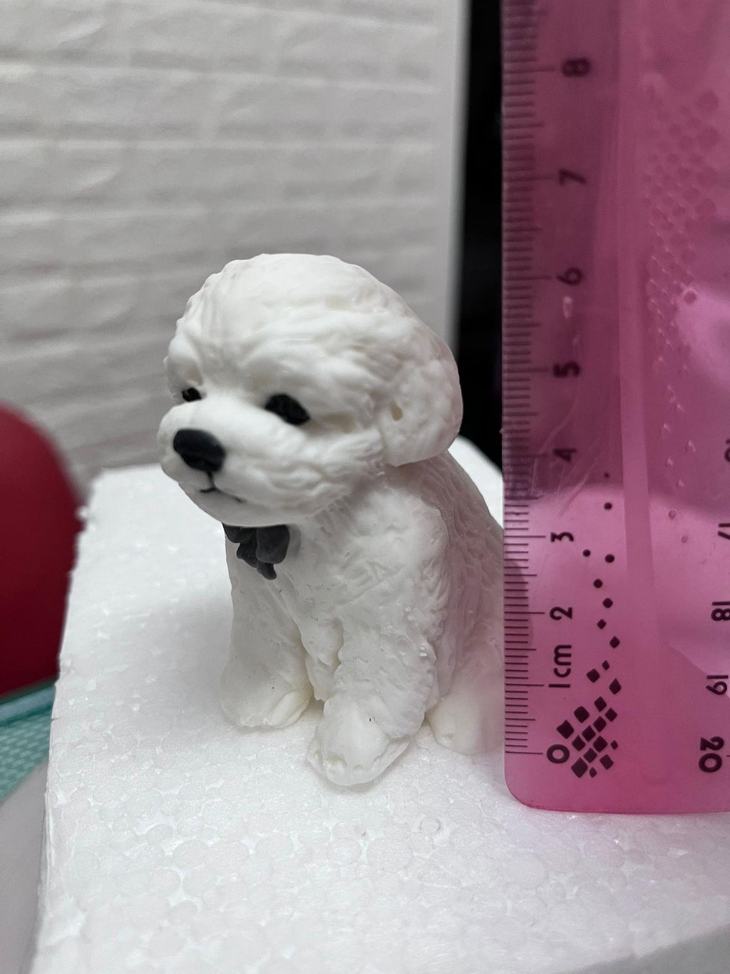 White edible fondant dog cake topper with a dark bow beside a ruler showing its height.