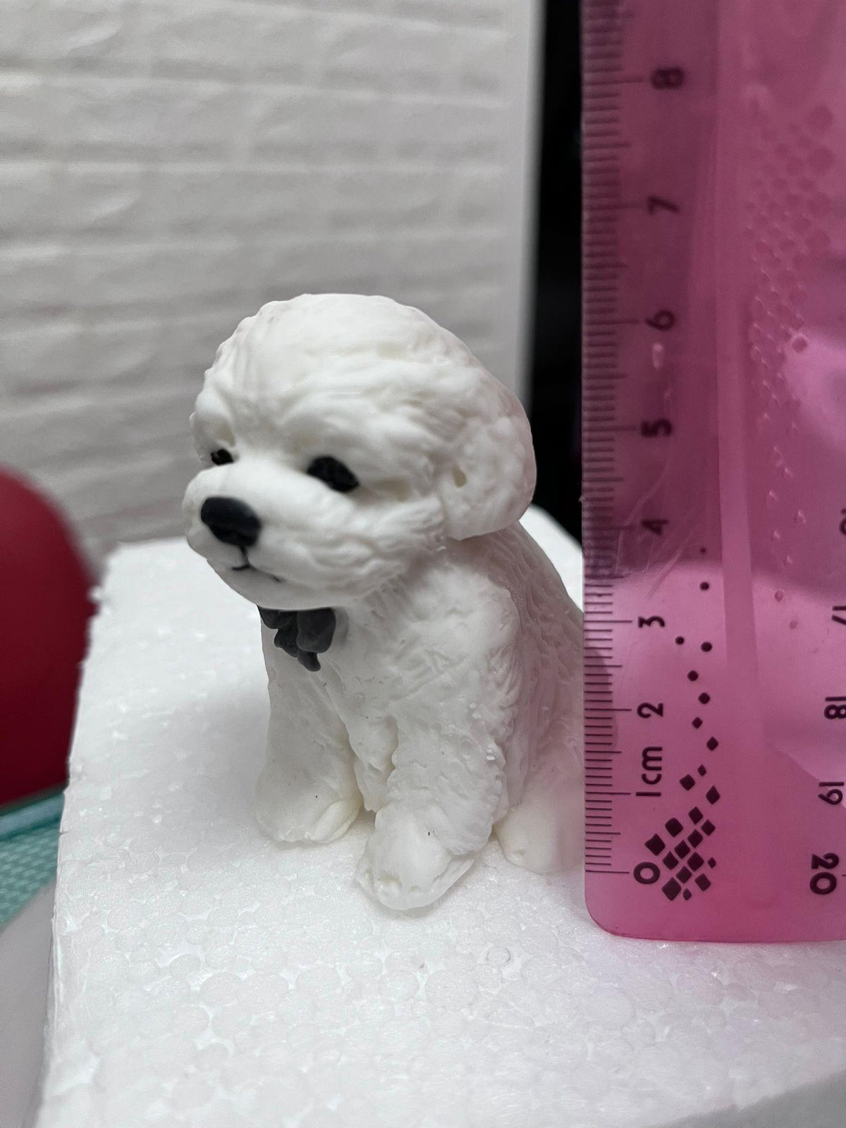 White edible fondant dog cake topper with a dark bow beside a ruler showing its height.