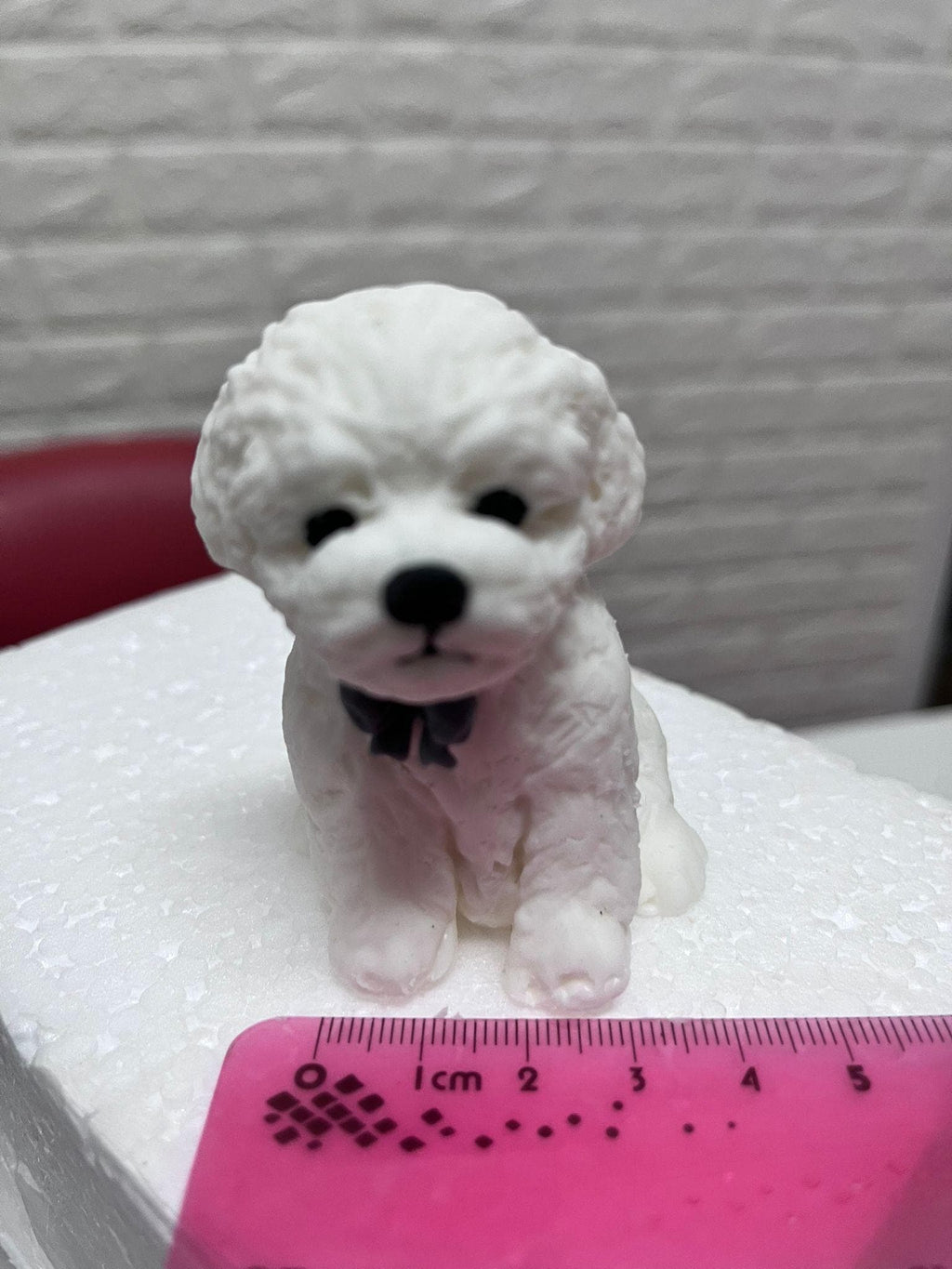 Front view of a white edible fondant dog cake topper with a ruler showing its width.