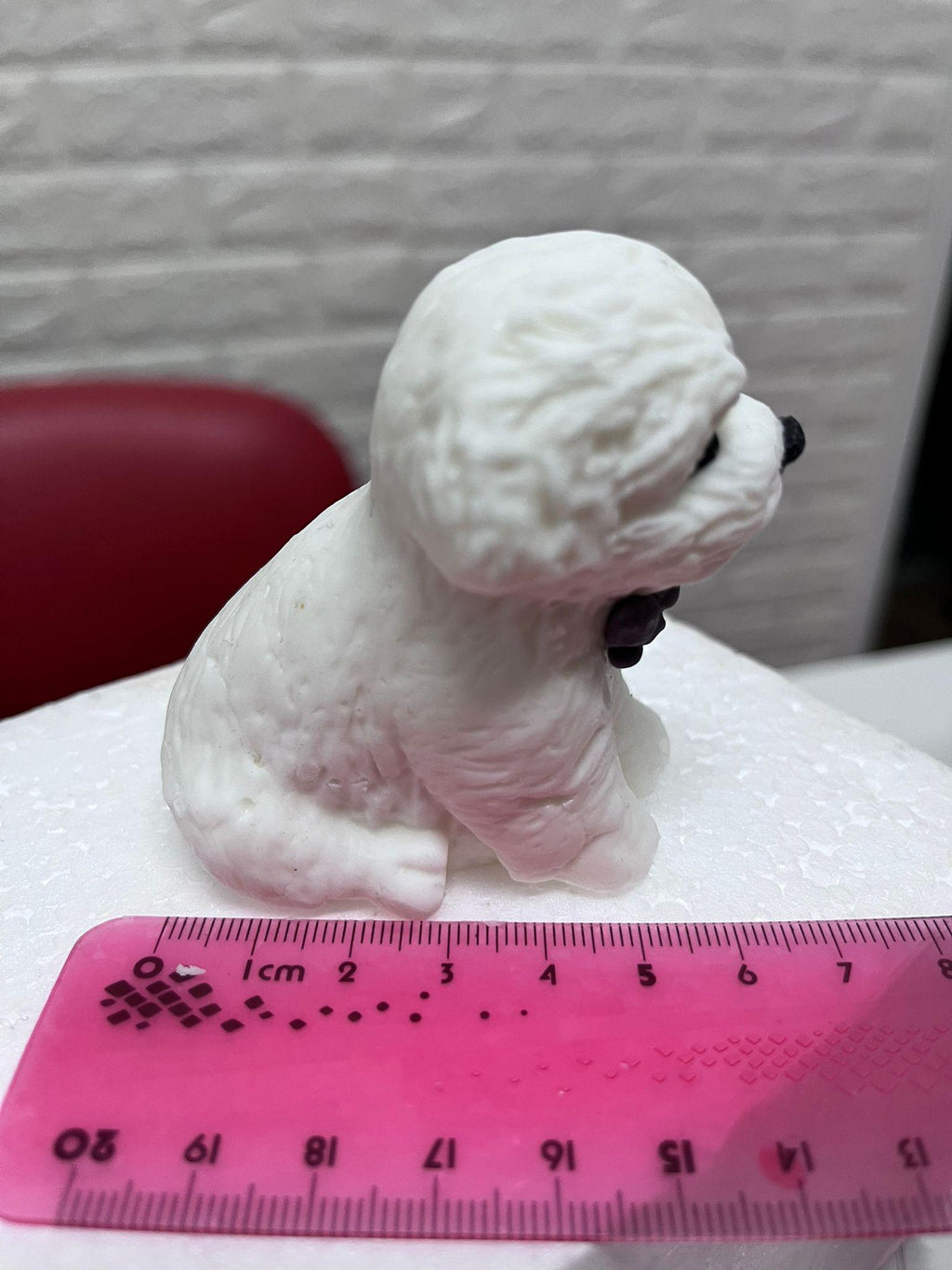 Side view of a white edible fondant dog cake topper with a curled tail, beside a ruler.
