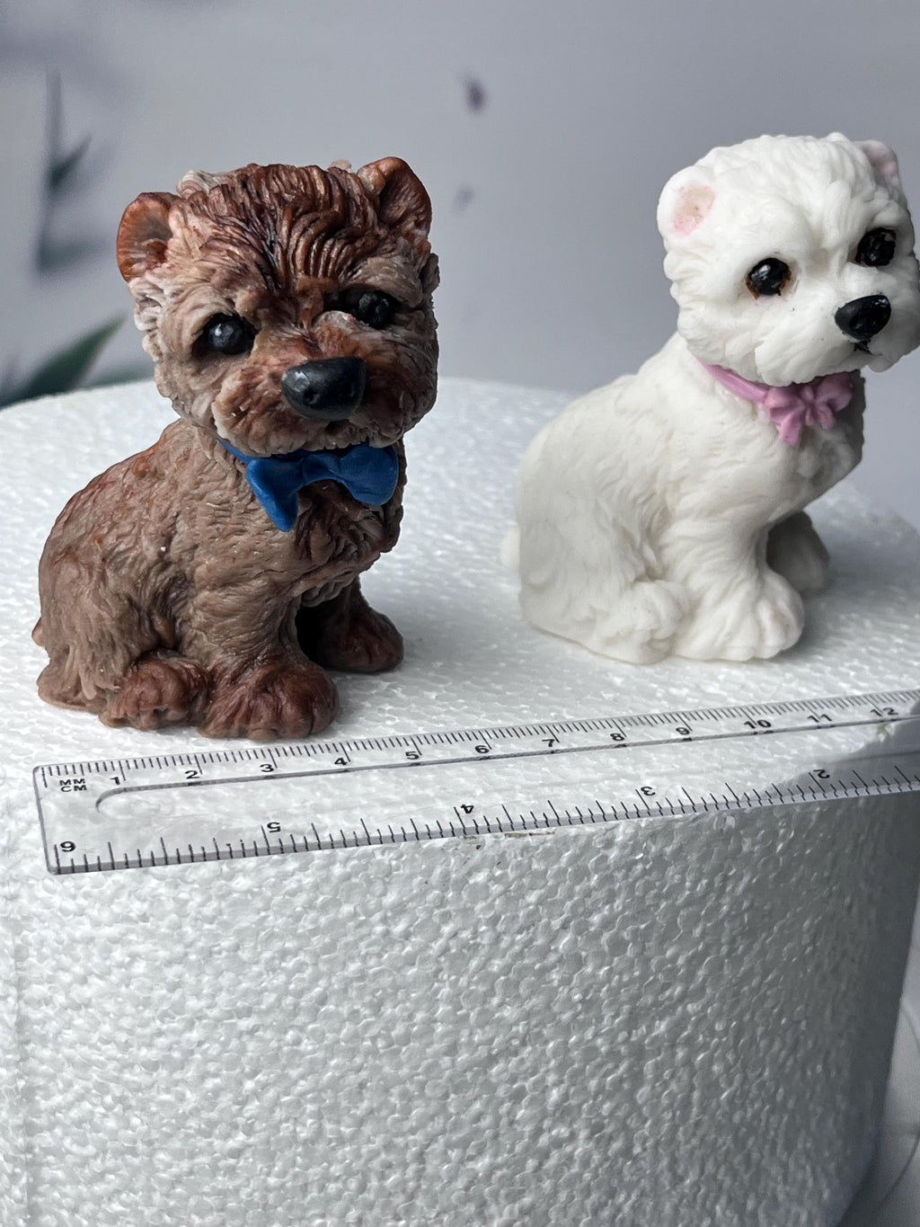 Brown and white edible fondant terrier dog cake toppers beside a ruler showing their size.