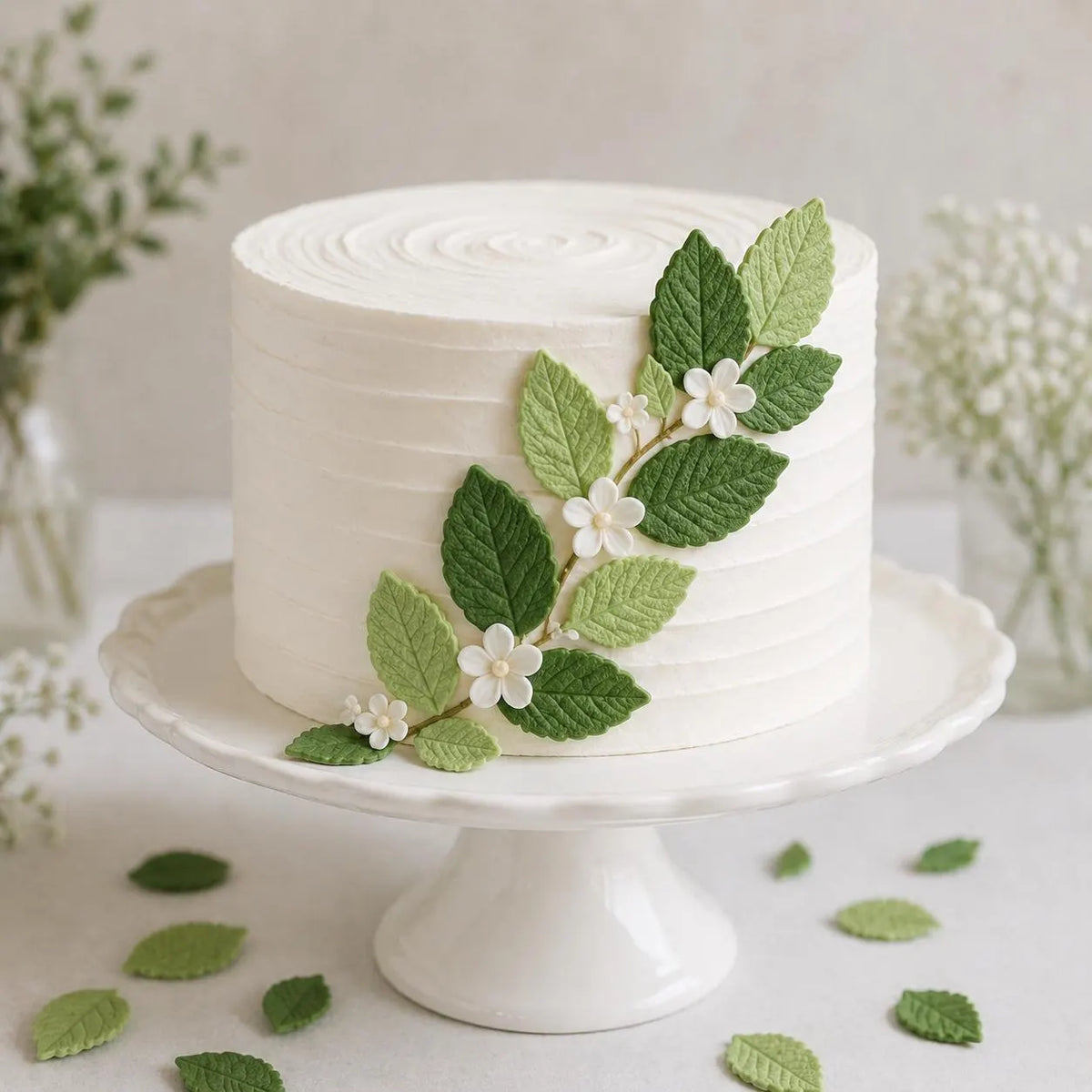 Green and light green edible sugar leaves arranged on a white celebration cake.