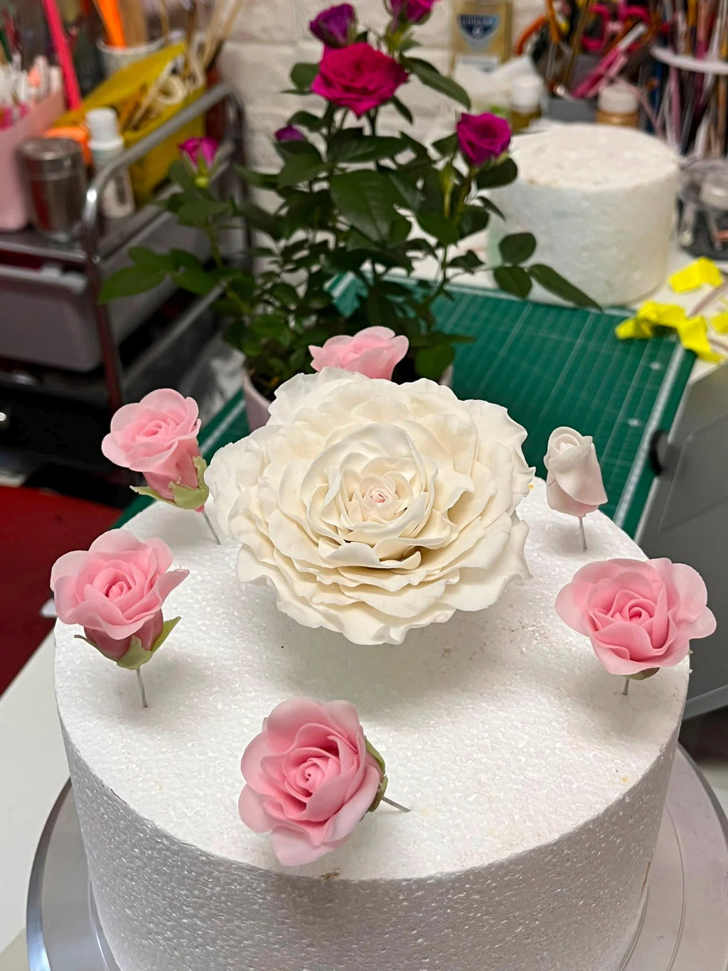 Ivory sugar rose surrounded by small pink roses on a celebration cake.