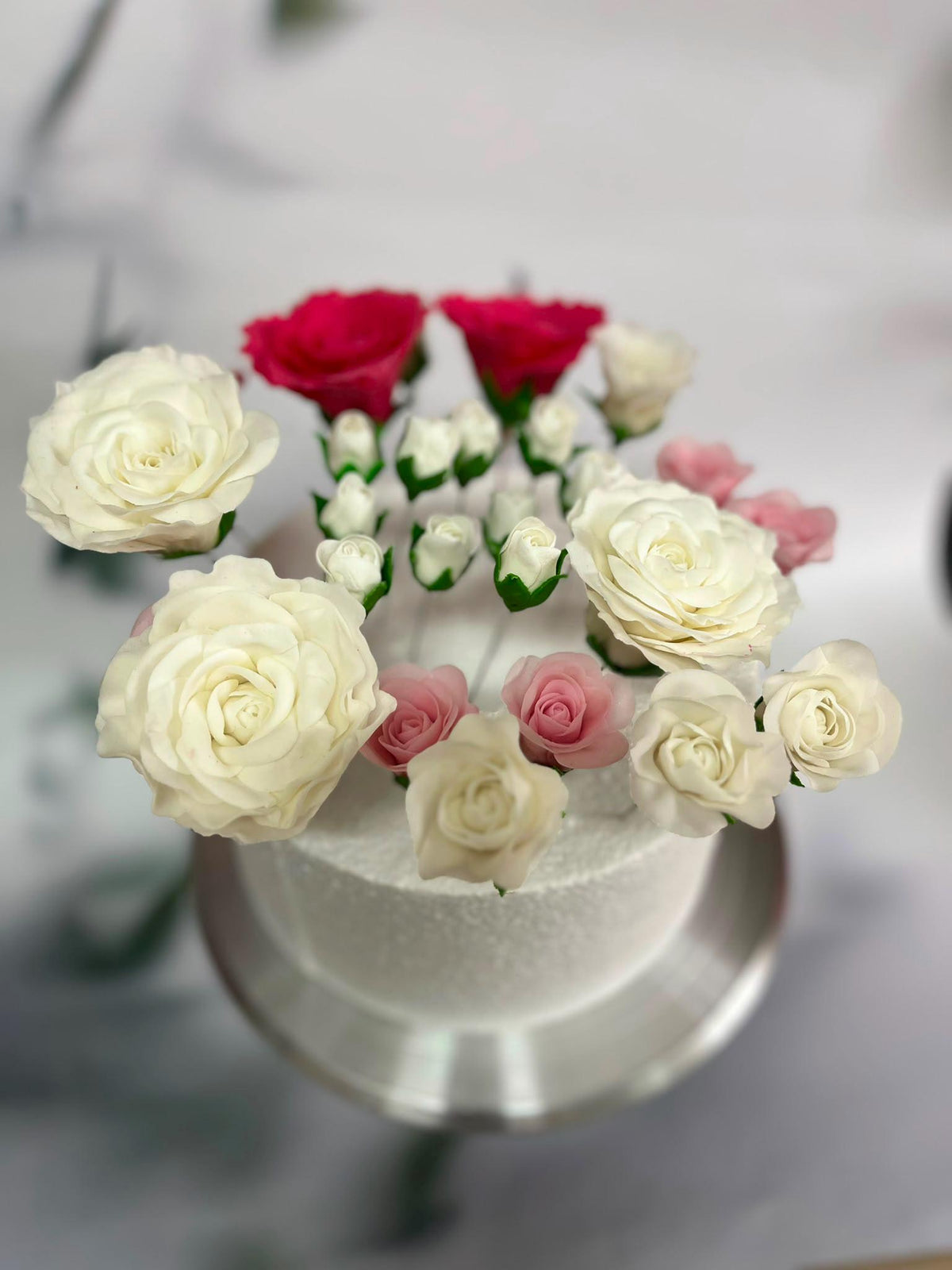 Ivory sugar roses with pink rosebuds and red flowers on a celebration cake.