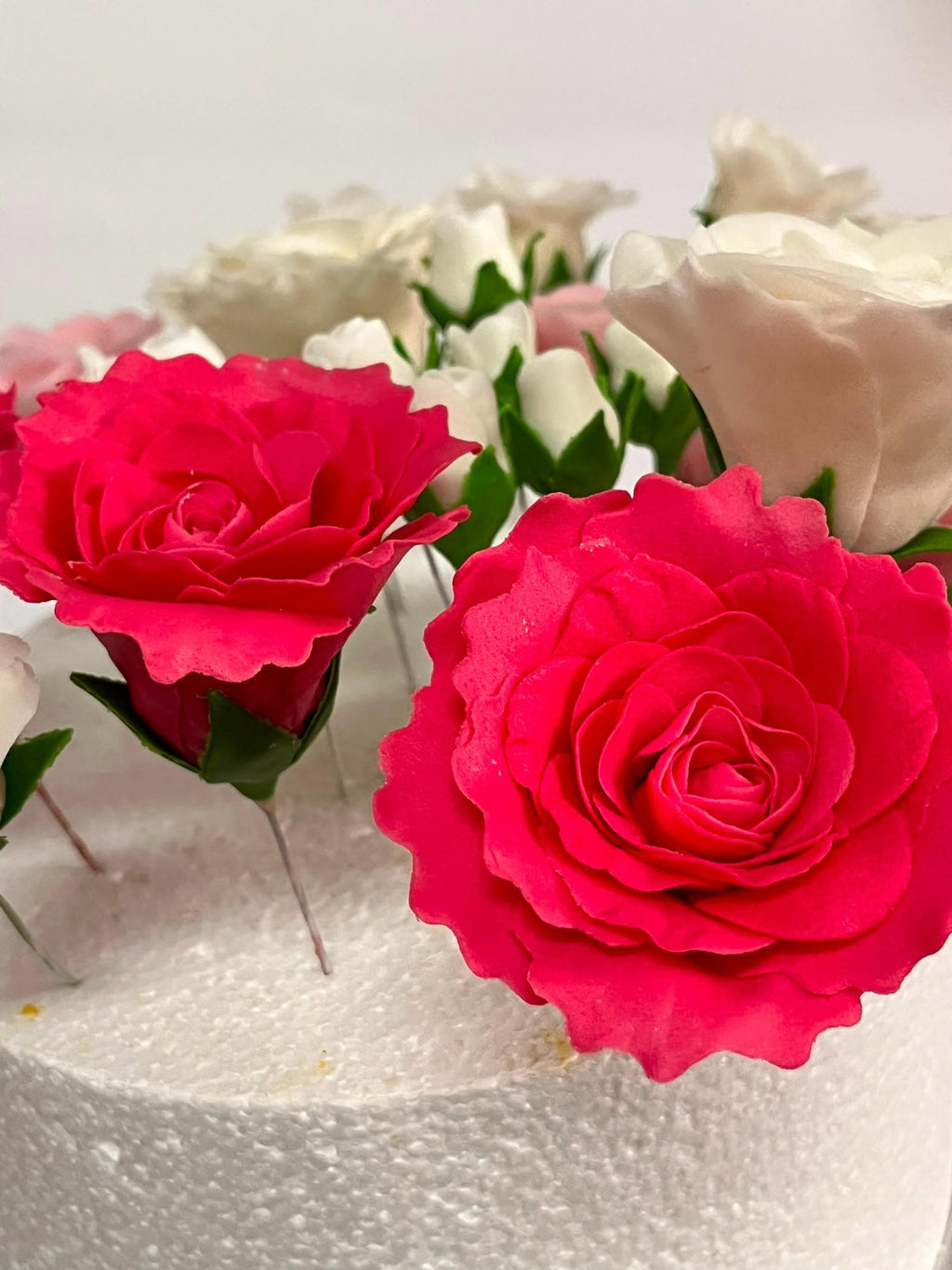 Large red sugar roses with green leaves decorating a white cake.