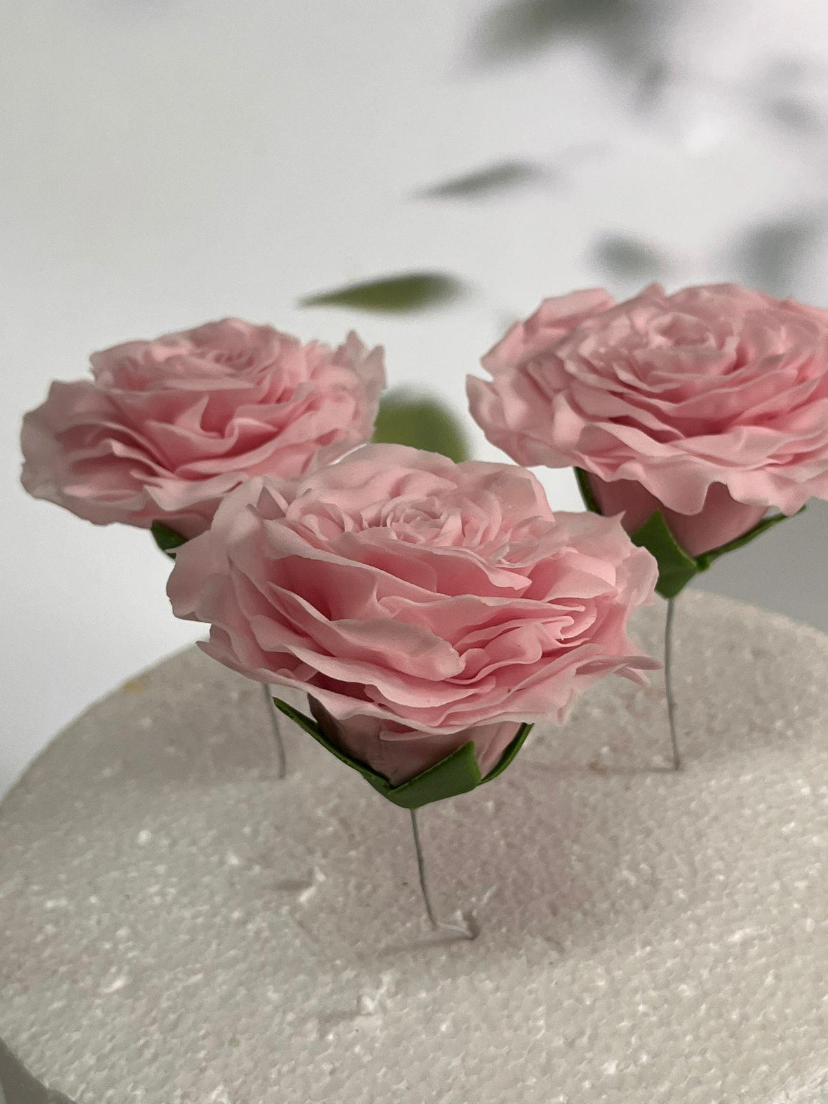 Pink edible sugar roses shown close up on a white cake.