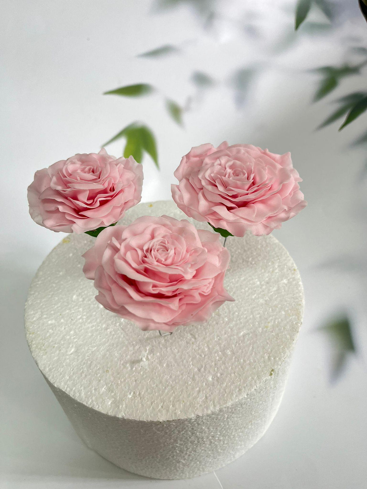 Three pink handmade sugar roses with green leaves.