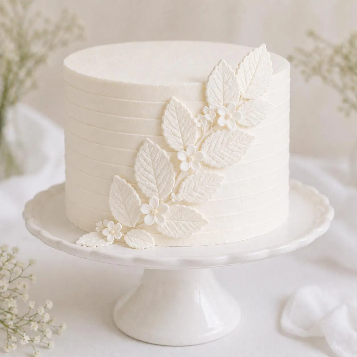 White handmade edible sugar leaves decorating a white wedding cake.