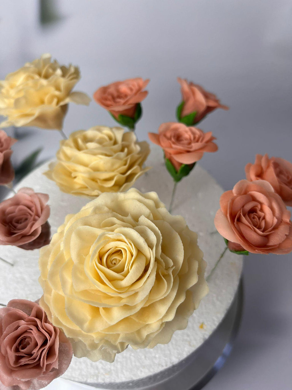 Yellow sugar roses and peach rosebuds arranged on a white cake.